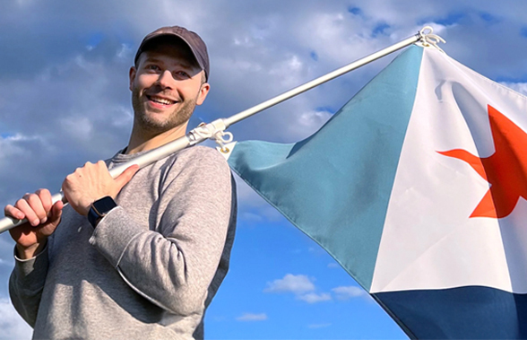 Eric Hart, designer of the new Syracuse city flag, smiling and holding the flag over his shoulder outdoors.