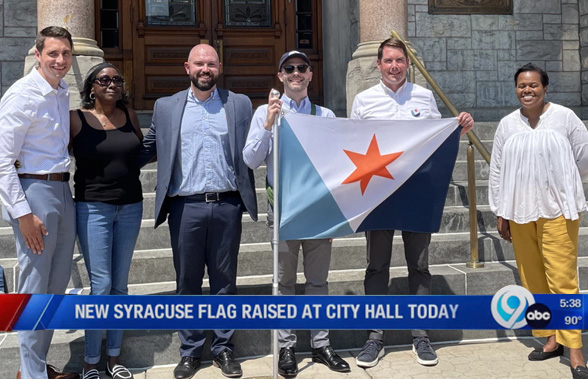 Eric Hart with the mayor and Syracuse city officials on the steps of City Hall, holding the new city flag on the day it was adopted.