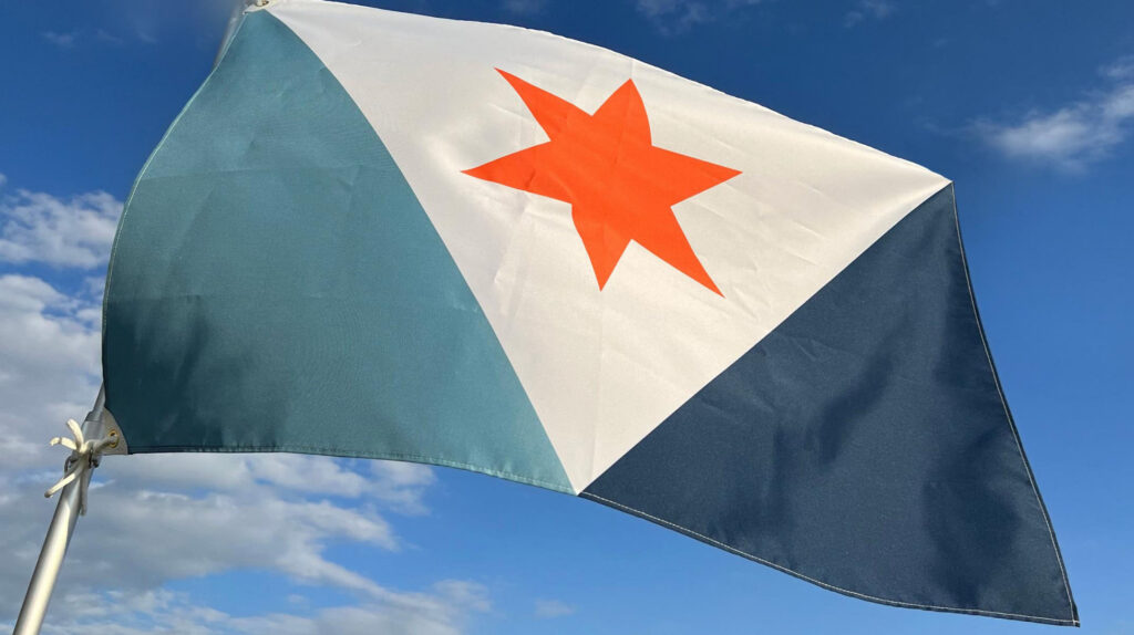 Close-up of the Syracuse city flag waving on a pole against a bright blue sky with scattered clouds.