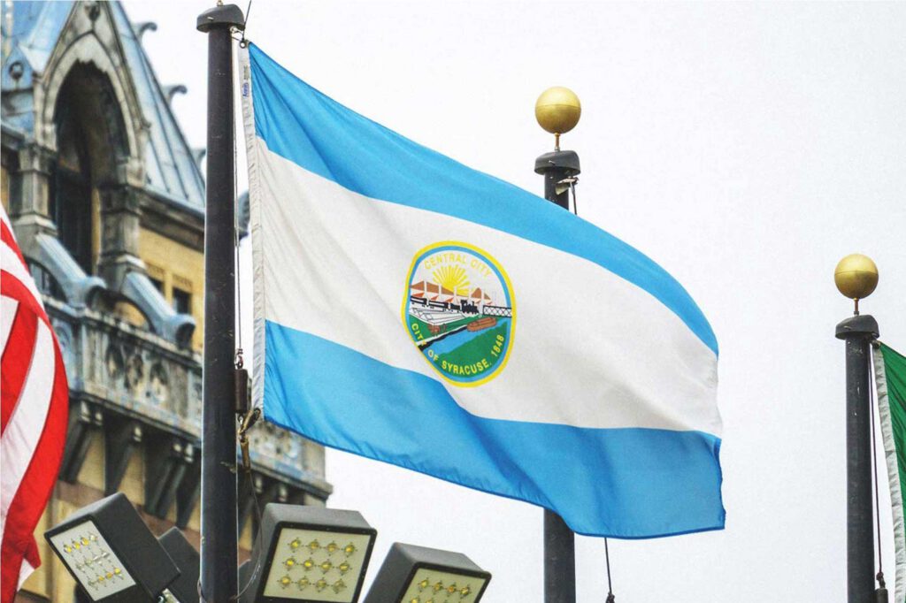 Original Syracuse city flag flying on a pole outside City Hall, with the city seal reading 'Central City, City of Syracuse 1848.'