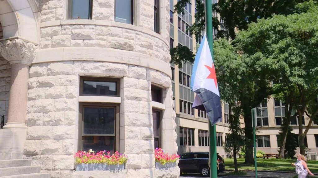 The newly raised Syracuse city flag flying on a green flagpole outside Syracuse City Hall