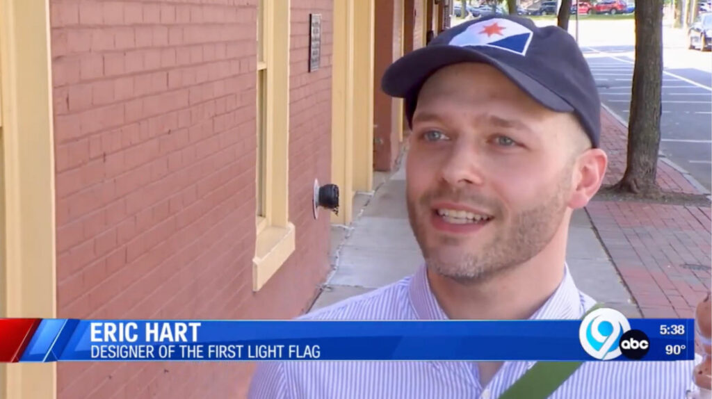 News Channel 9 outdoor interview still of Eric Hart wearing a Syracuse city flag baseball cap, smiling while speaking.